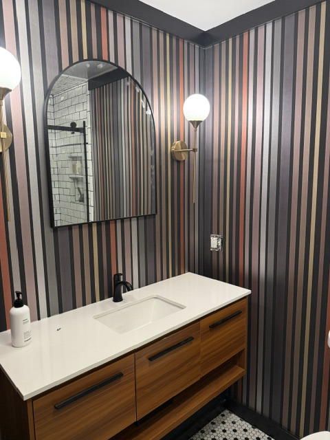 Bathroom with striped wallpaper, walnut vanity and brass sconces